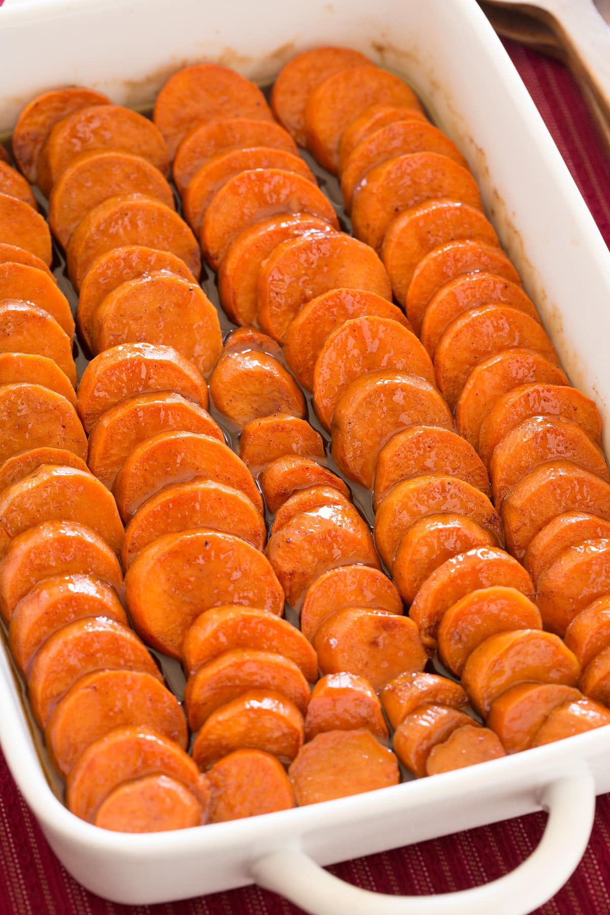Candied yams. Sweet potatoes are shown in rows in a casserole dish, they are coated in a butter, brown sugar sauce.