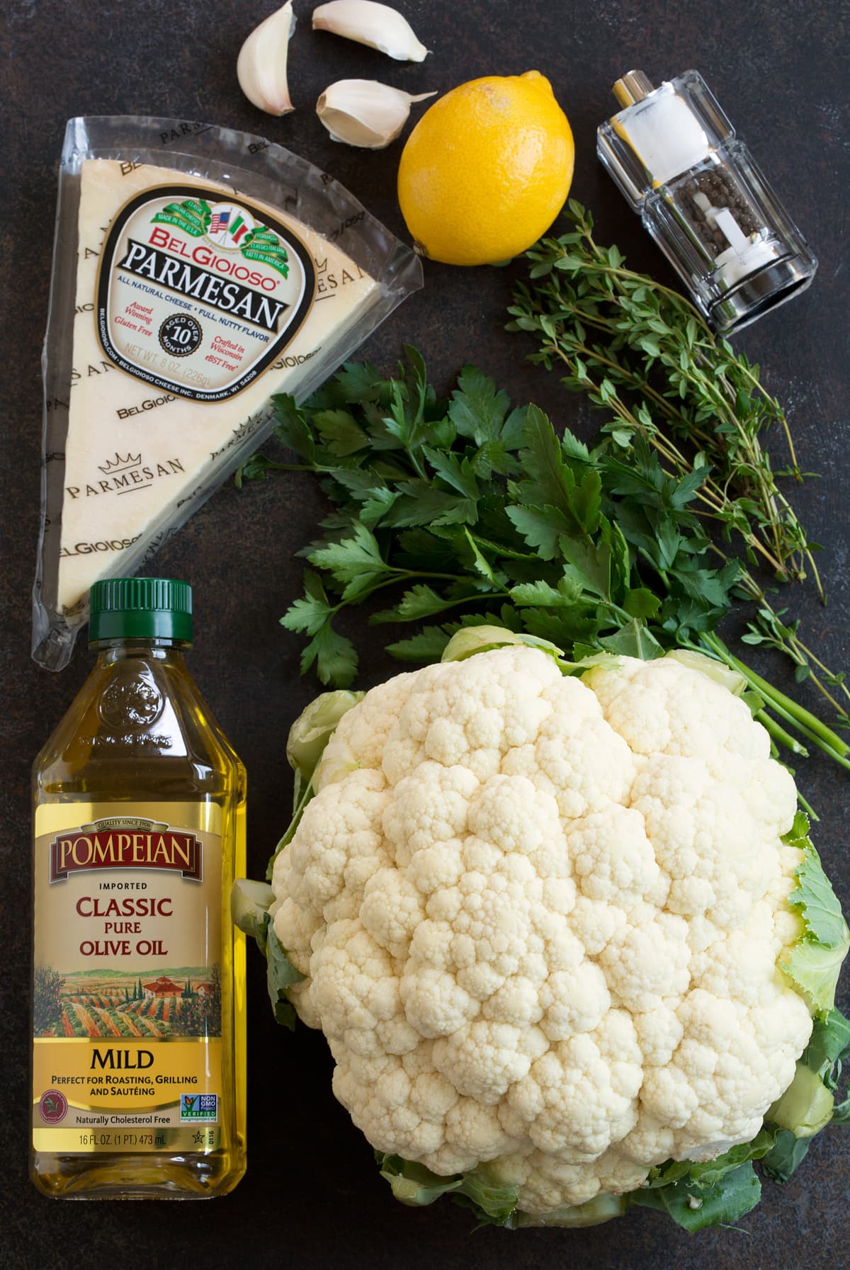 Image of ingredients used to make roasted cauliflower. Includes whole head of cauliflower, olive oil, salt and pepper then optional seasonings garlic, lemon, parmesan and fresh herbs.