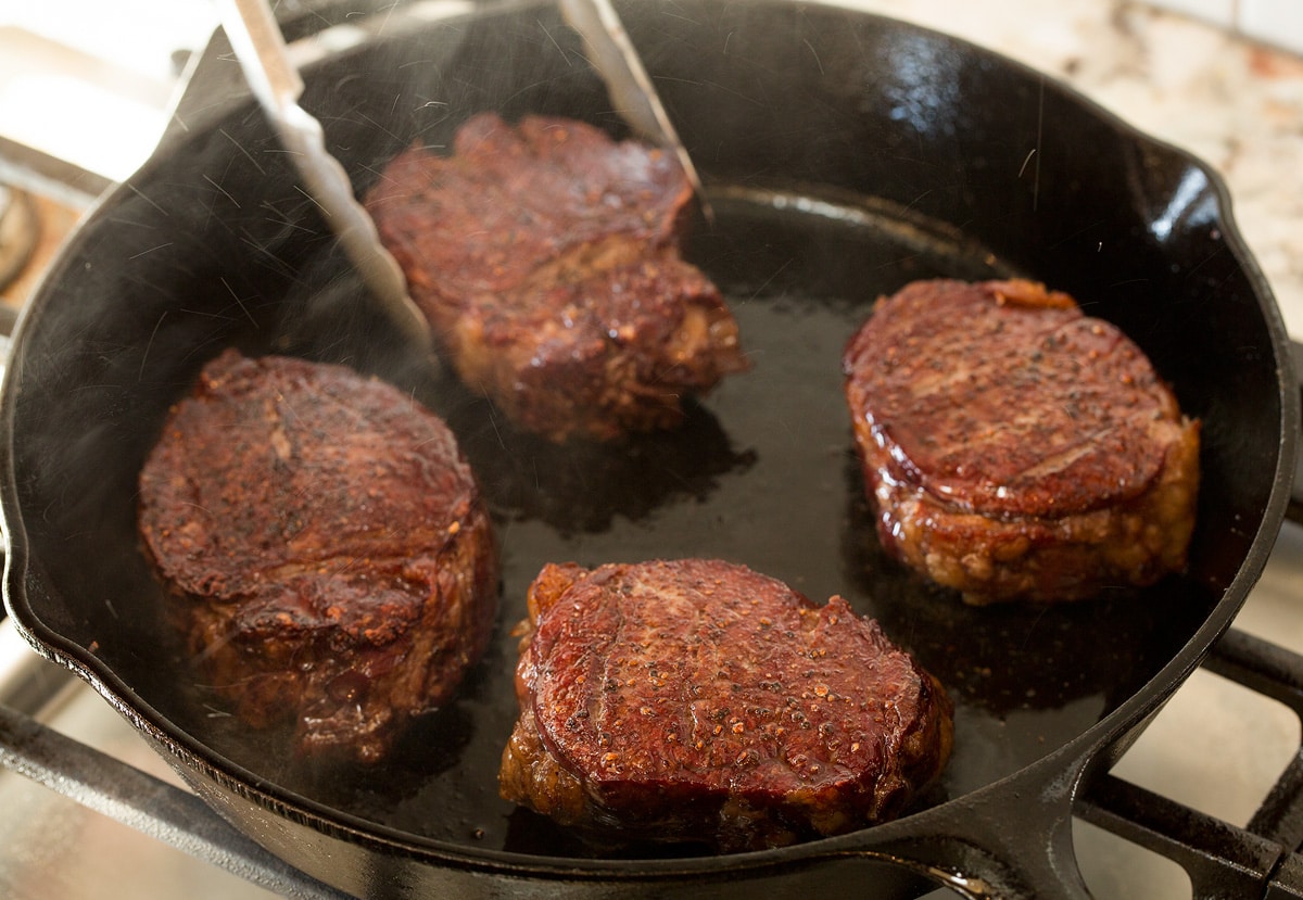 Showing how to reverse sear steaks in a cast iron skillet on stovetop.