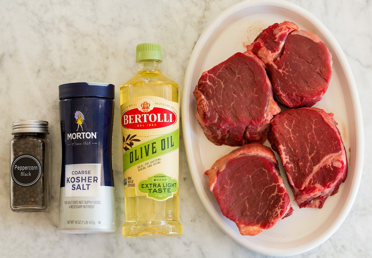 Photo of ingredients for filet mignon. Includes four medium filet mignon steaks, light olive oil, kosher salt and black pepper.