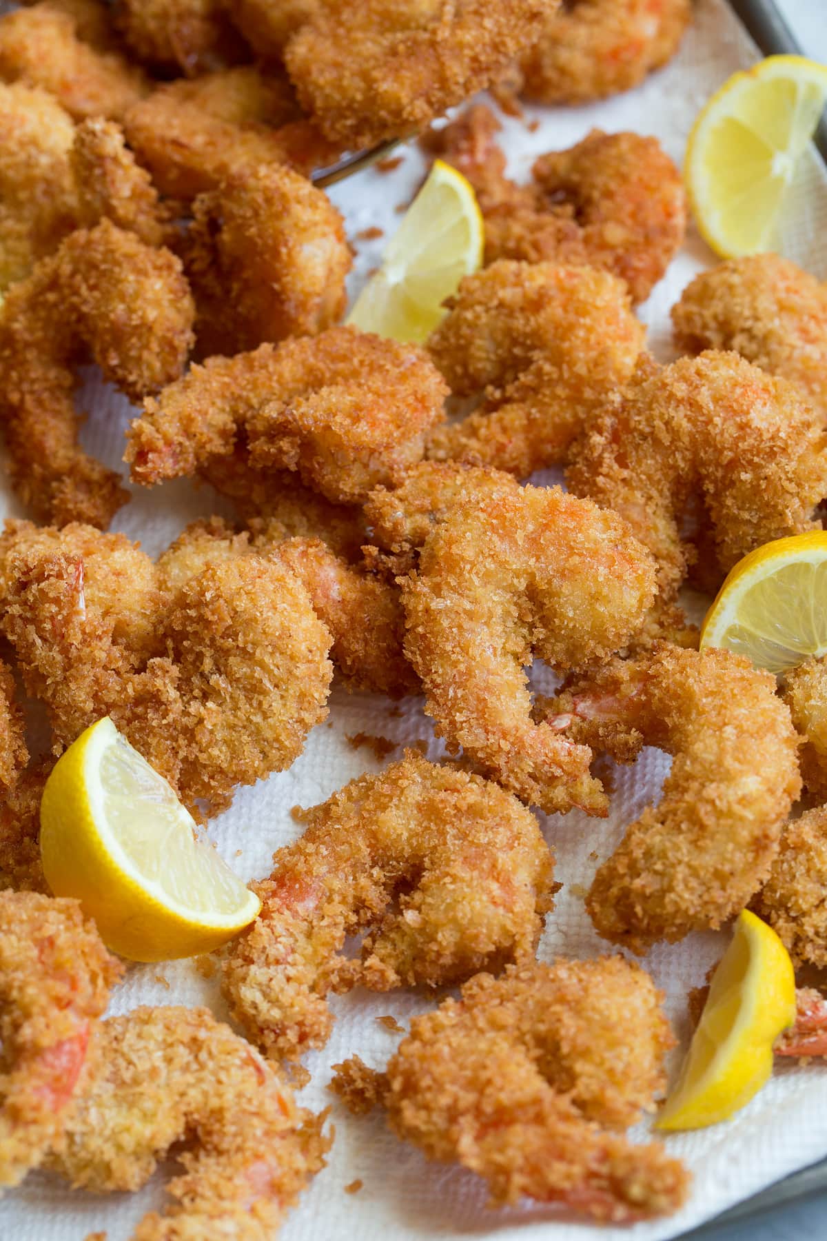 Close up photo of panko crusted fried shrimp piled on paper towel lined sheet pan.