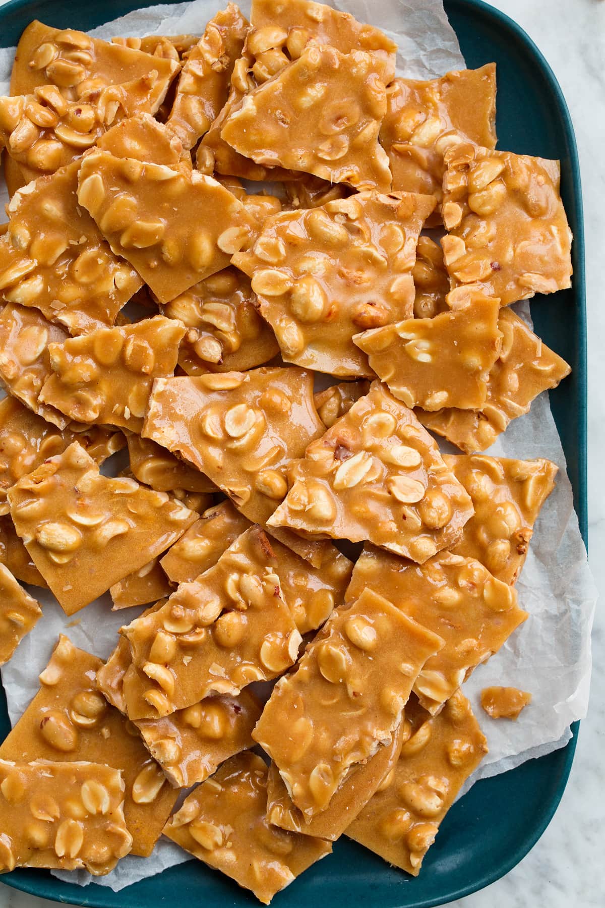 Close up overhead image of peanut brittle stacked on a blue platter with parchment paper.