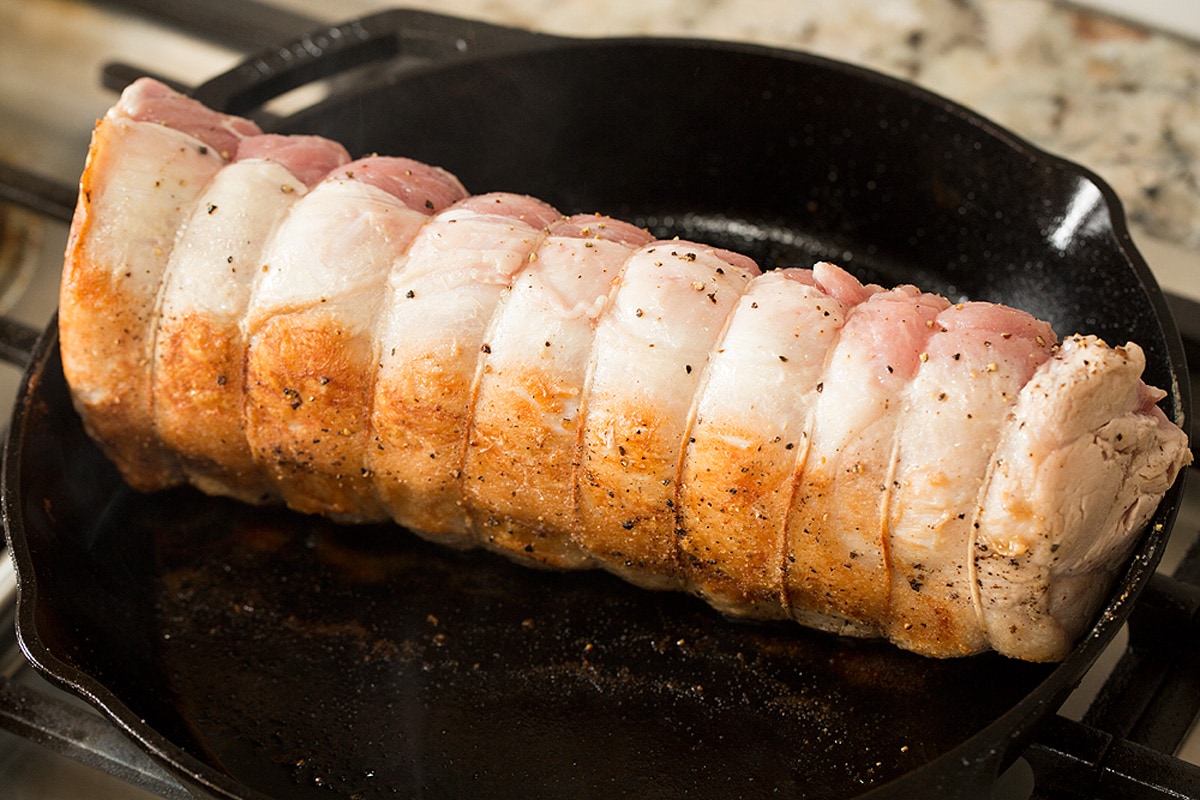 Pork loin being seared and browned in a cast iron skillet on the stovetop.
