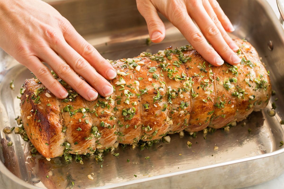 Rubbing herbs and garlic over pork loin in a roasting pan.