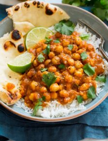 Photo of chickpea curry in a bowl served atop basmati rice with naan bread to the side.