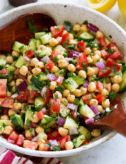 Chickpea Salad shown in a serving bowl with wooden serving spoons.