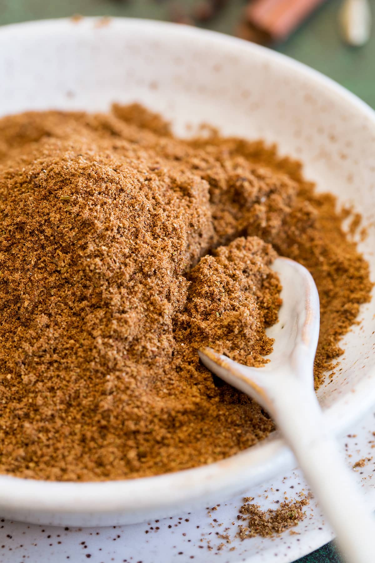 Garam masala spice blend shown up close in a bowl with a small spoon.