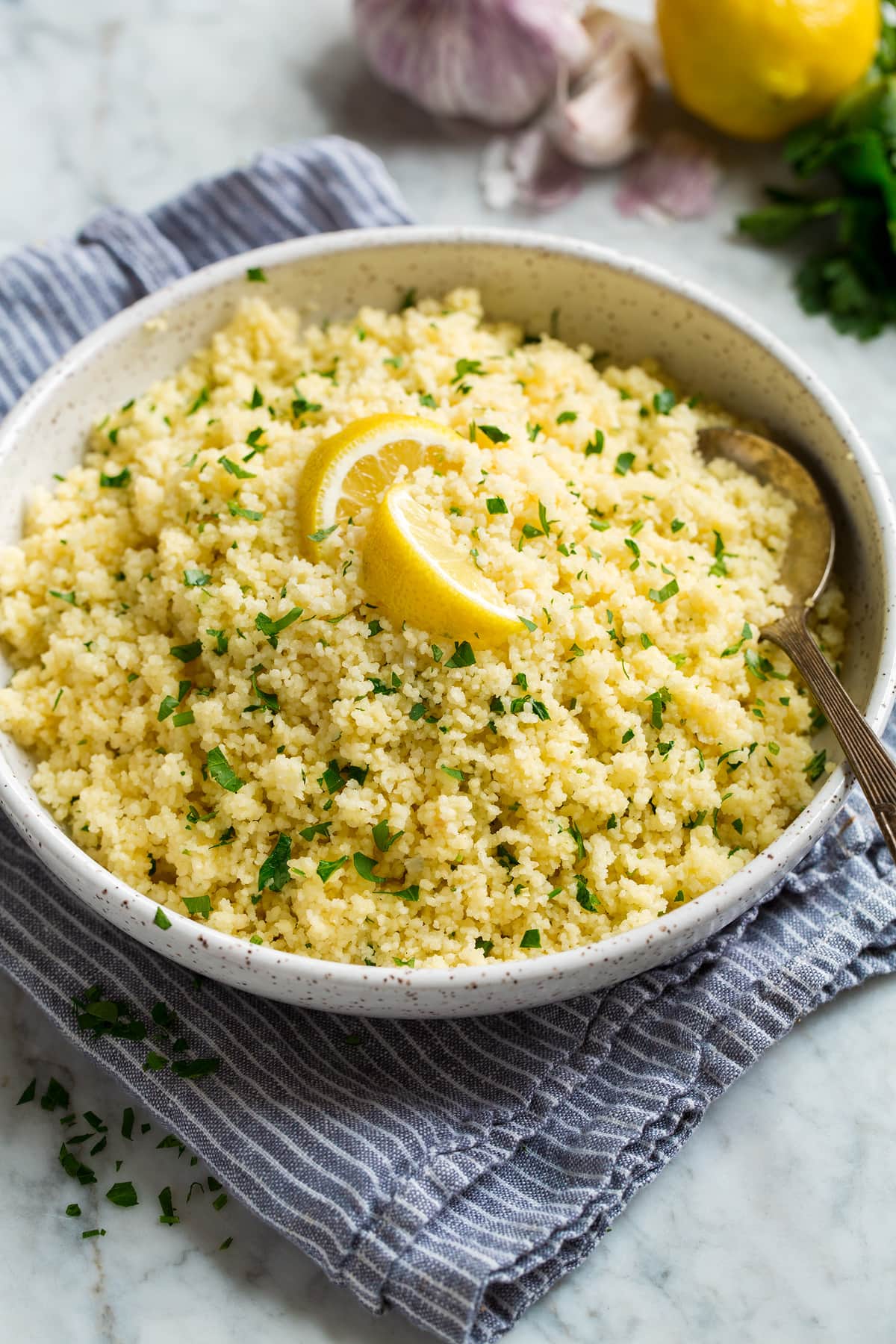 Lemon couscous shown in a white bowl over a grey striped cloth.