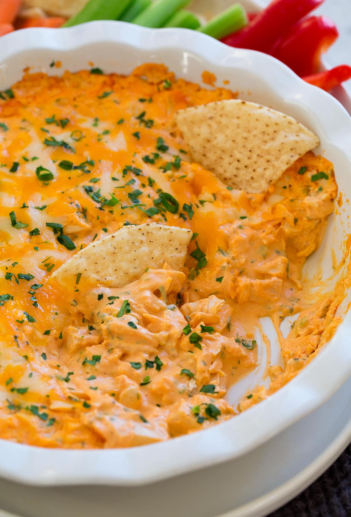 Buffalo chicken dip in a ceramic white pie dish. Shown with tortilla chips dipped in.