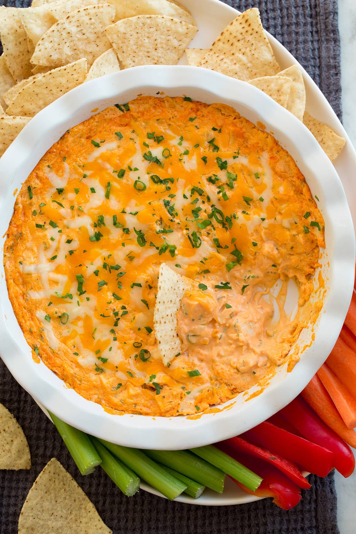 Overhead photo of buffalo chicken dip shown with serving suggestions on the side of carrots, bell pepper, celery and tortilla chips.