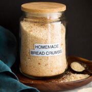 Image: homemade plain bread crumbs in a glass jar set on a wooden plate with a black background.