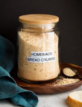 Image: homemade plain bread crumbs in a glass jar set on a wooden plate with a black background.