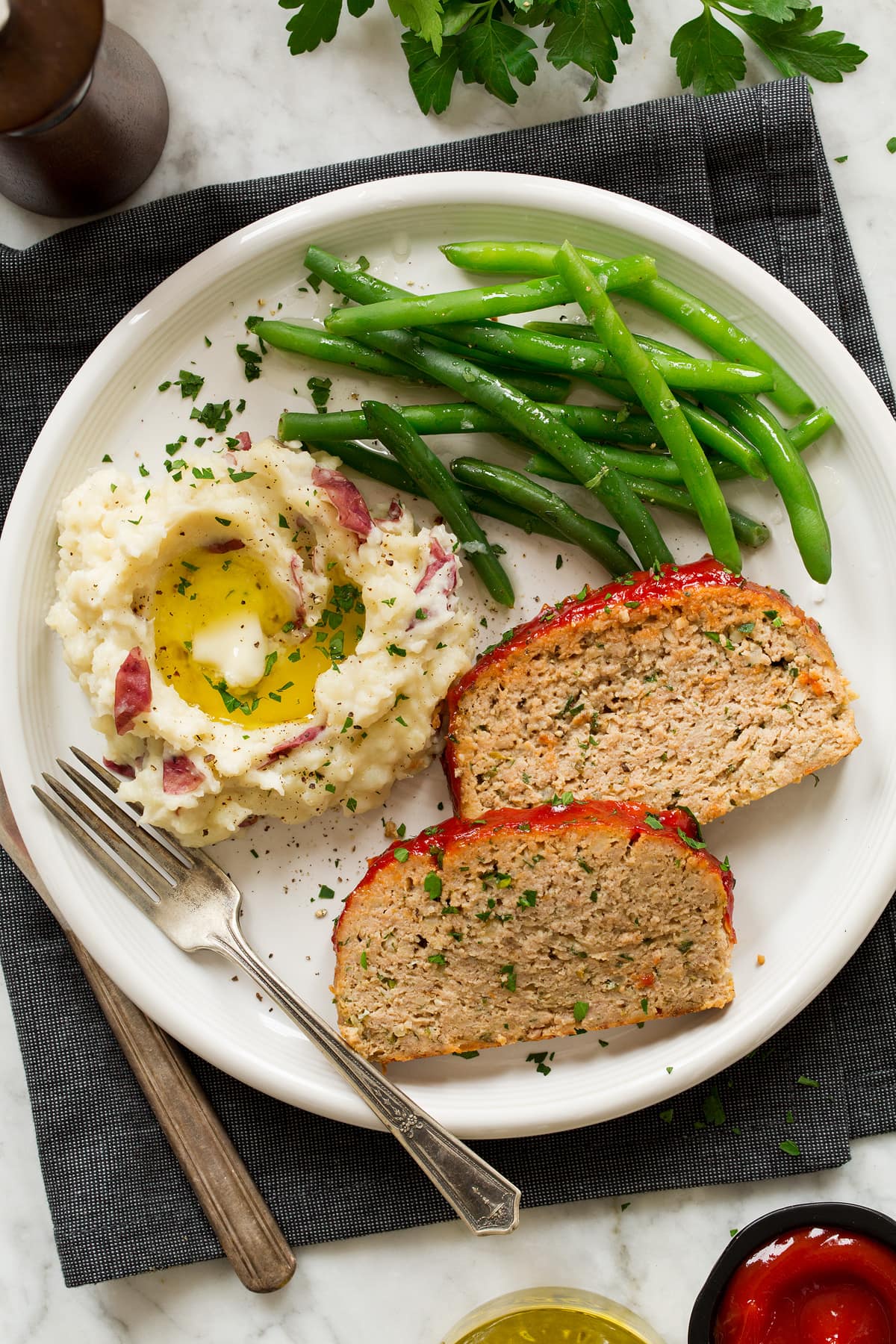 Two slices of turkey meatloaf shown on a serving plate with serving suggestions of mashed potatoes and green beans.