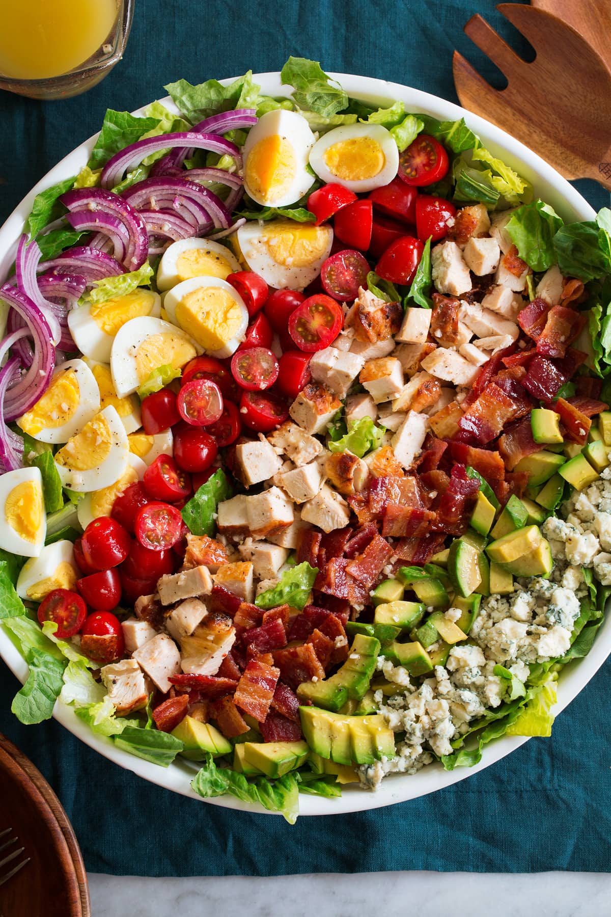 Overhead photo of cobb salad with blue cheese, avocado, bacon, chicken, tomatoes, hard boiled eggs, red onion and romaine lettuce in a large white bowl.