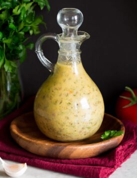 Photo: Italian Dressing in a glass bottle set over a wooden plate and a red cloth.