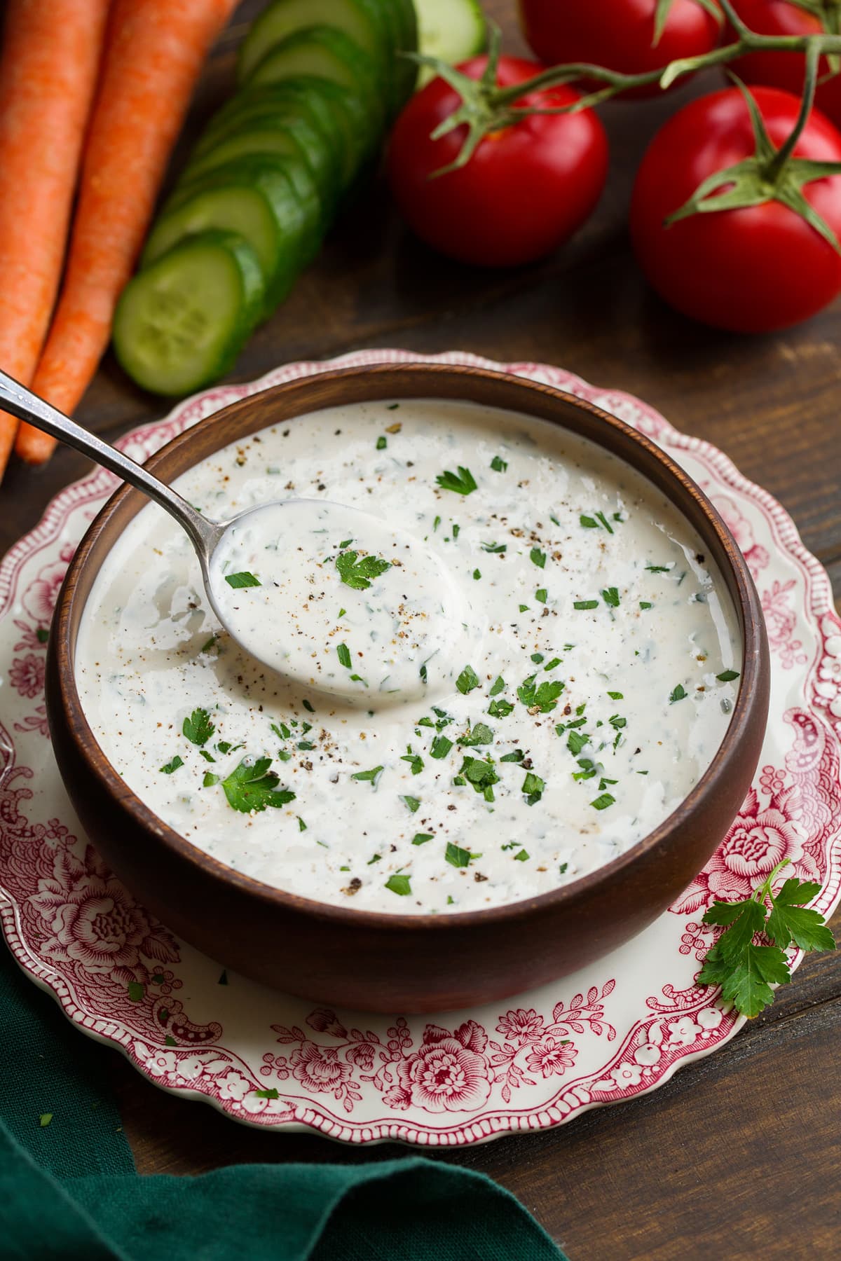 Photo of ranch dressing in a wooden bowl with fresh veggies in the background.