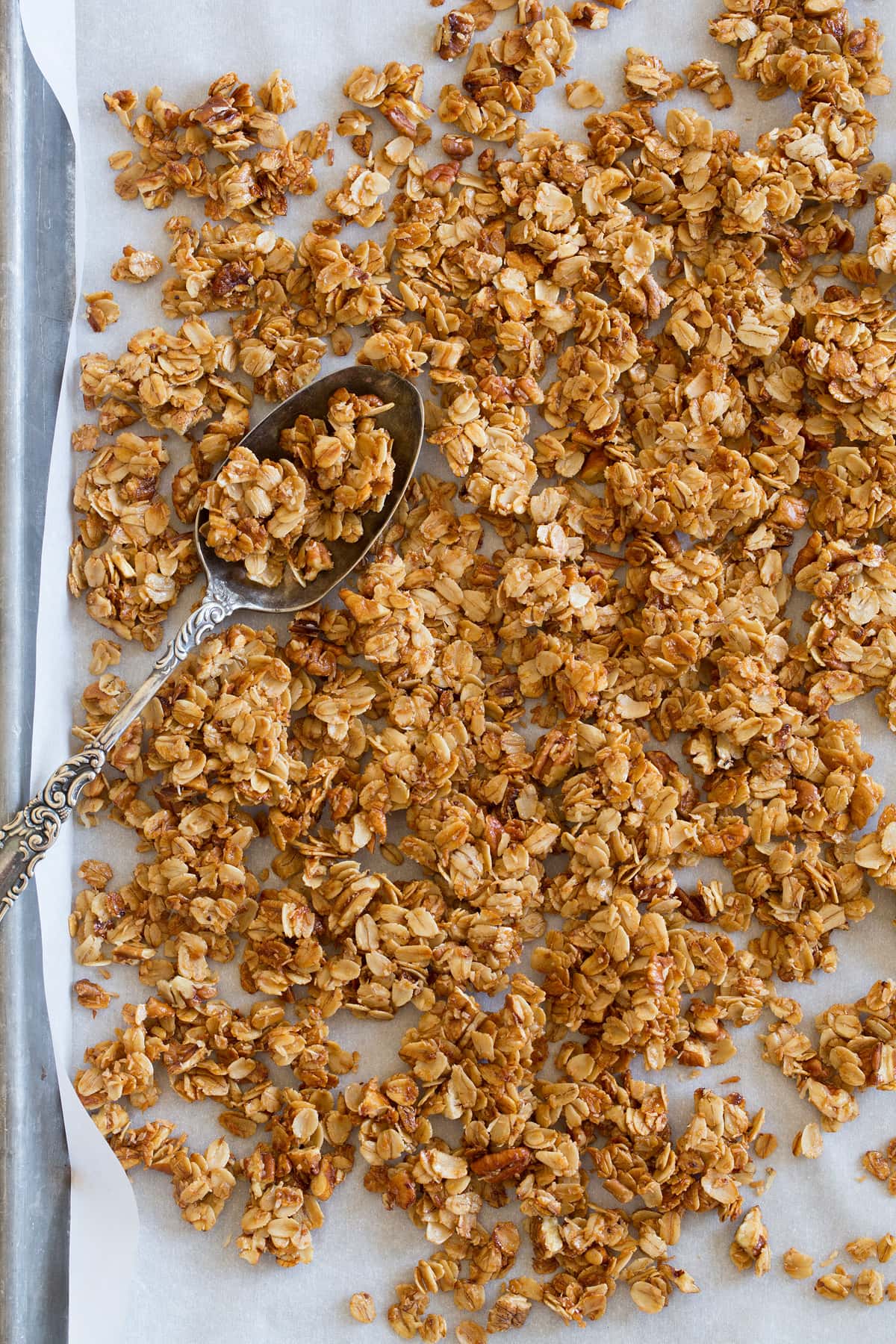 Homemade granola recipe shown spread out on a baking sheet with parchment paper.