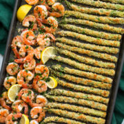 Photo of sheet pan filled with a row of garlic lemon butter shrimp on the left side and panko parmesan crusted asparagus on the ride side. Shown from overhead.
