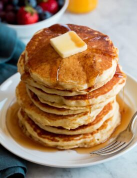 Stack of homemade pancakes on a white plate. Pancakes are topped with maple syrup and butter.