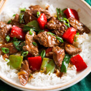 Photo: Pepper Steak in a bowl over white rice. Bowl is resting on a dark green cloth over a marble surface.