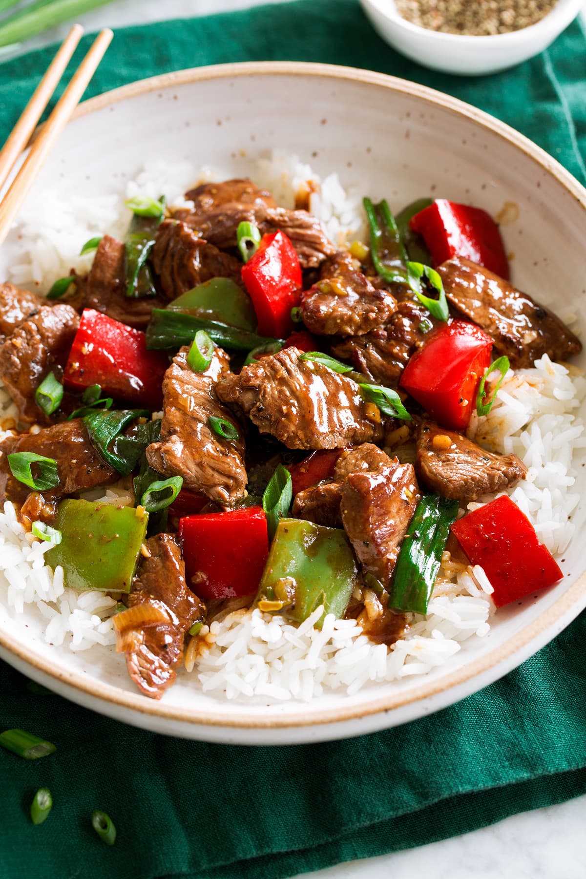 Photo: Pepper Steak in a bowl over white rice. Bowl is resting on a dark green cloth over a marble surface.