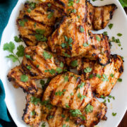 Yogurt Marinated Grilled Chicken shown from above on a white oval platter on a wooden table with a turquoise cloth to the side.