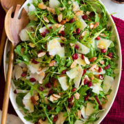 Arugula salad on a white oval platter over a red cloth.