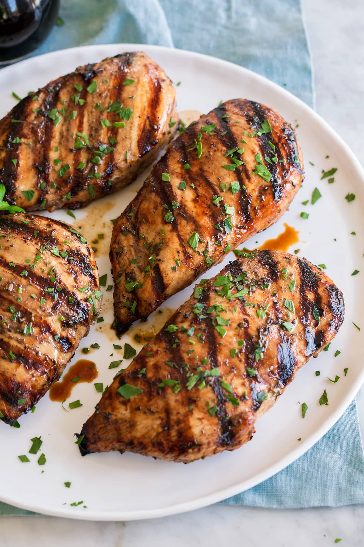 Balsamic chicken breasts shown on a white plate over a blue cloth on a marble surface.
