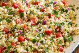 Couscous salad with cucumbers, tomatoes, and herbs shown in a white bowl from the side.