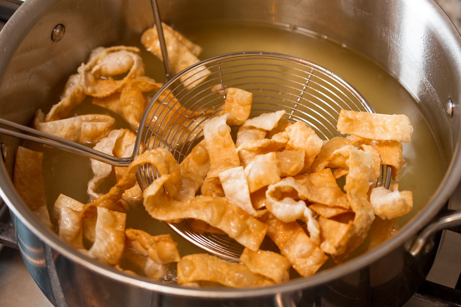 Golden brown fried wonton strips being removed from oil.