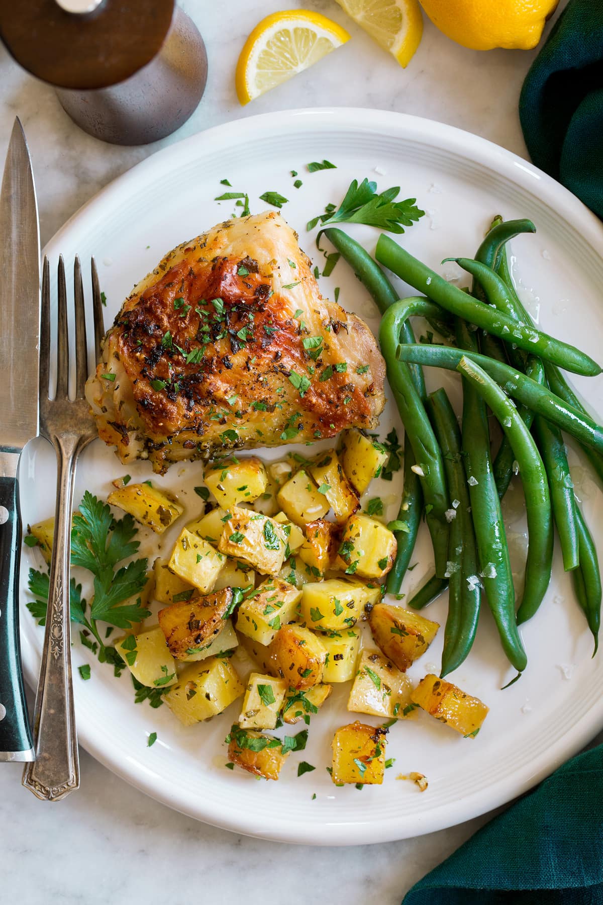 A dish with baked chicken thighs and potatoes with a side of green beans. Shown from above.