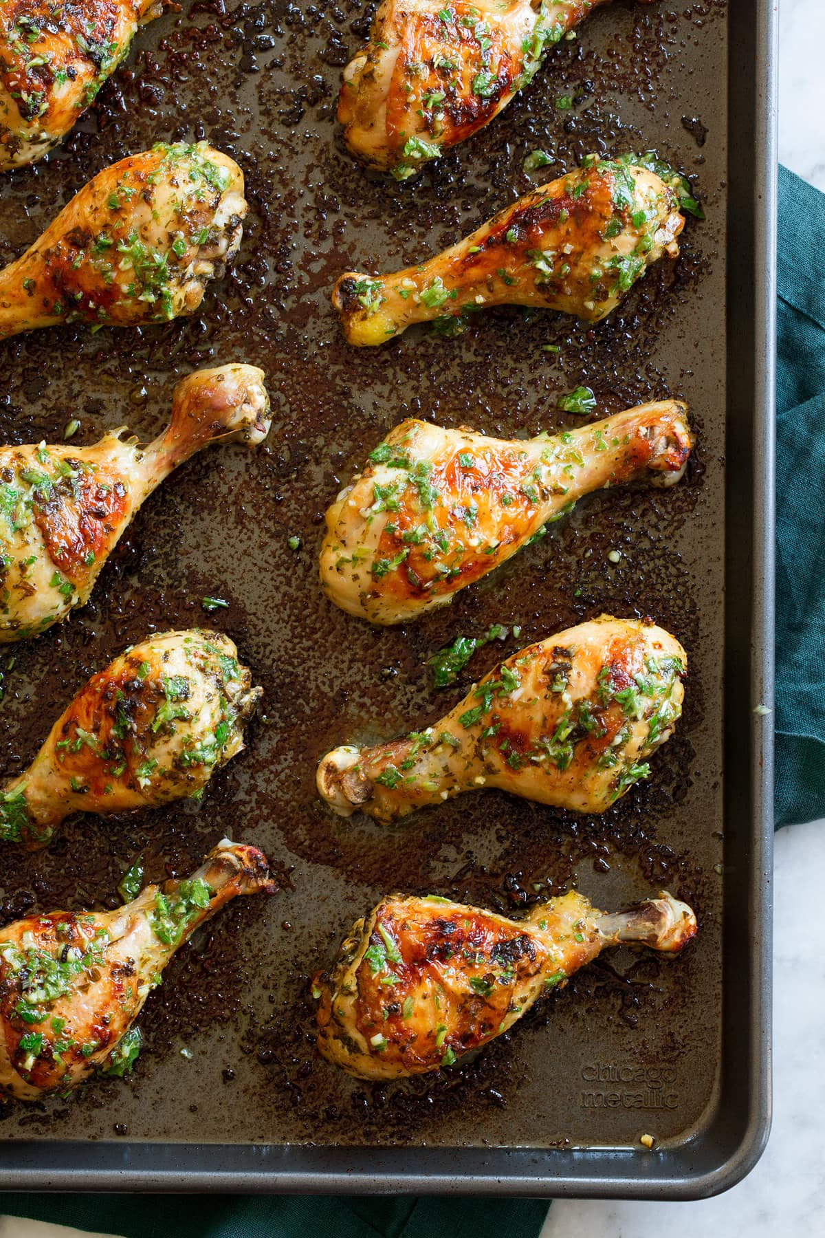 Chicken legs shown on baking sheet covered with chimichurri style sauce.