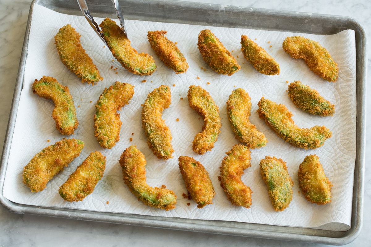 Avocado fries draining on paper towel lined baking sheet.