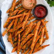 Baked sweet potato fries on a white oval platter with dipping sauces on the side.
