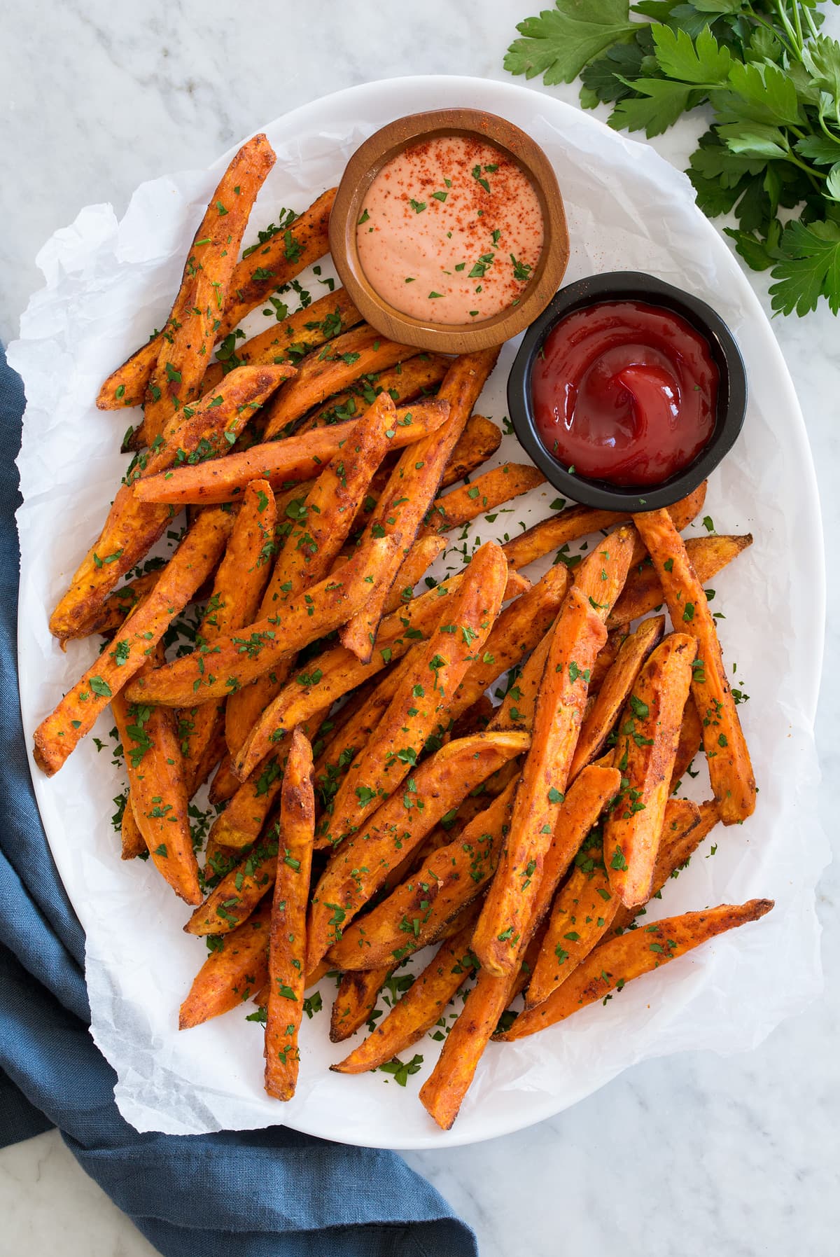 Baked sweet potato fries on a white oval platter with dipping sauces on the side.