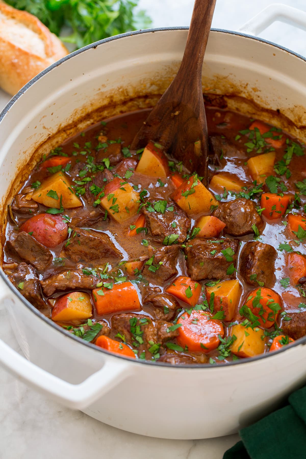 Beef stew with potatoes, carrots and chuck roast in a pot with a wooden spoon, it is shown from the side.