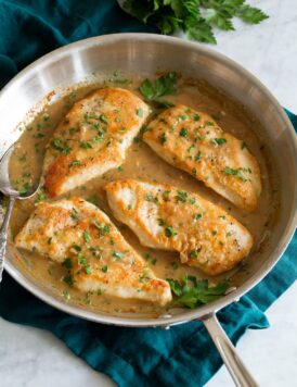 Chicken breasts in white wine and onion sauce in a skillet.