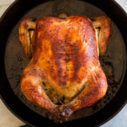 Whole brined and roast chicken shown overhead in a cast iron skillet.