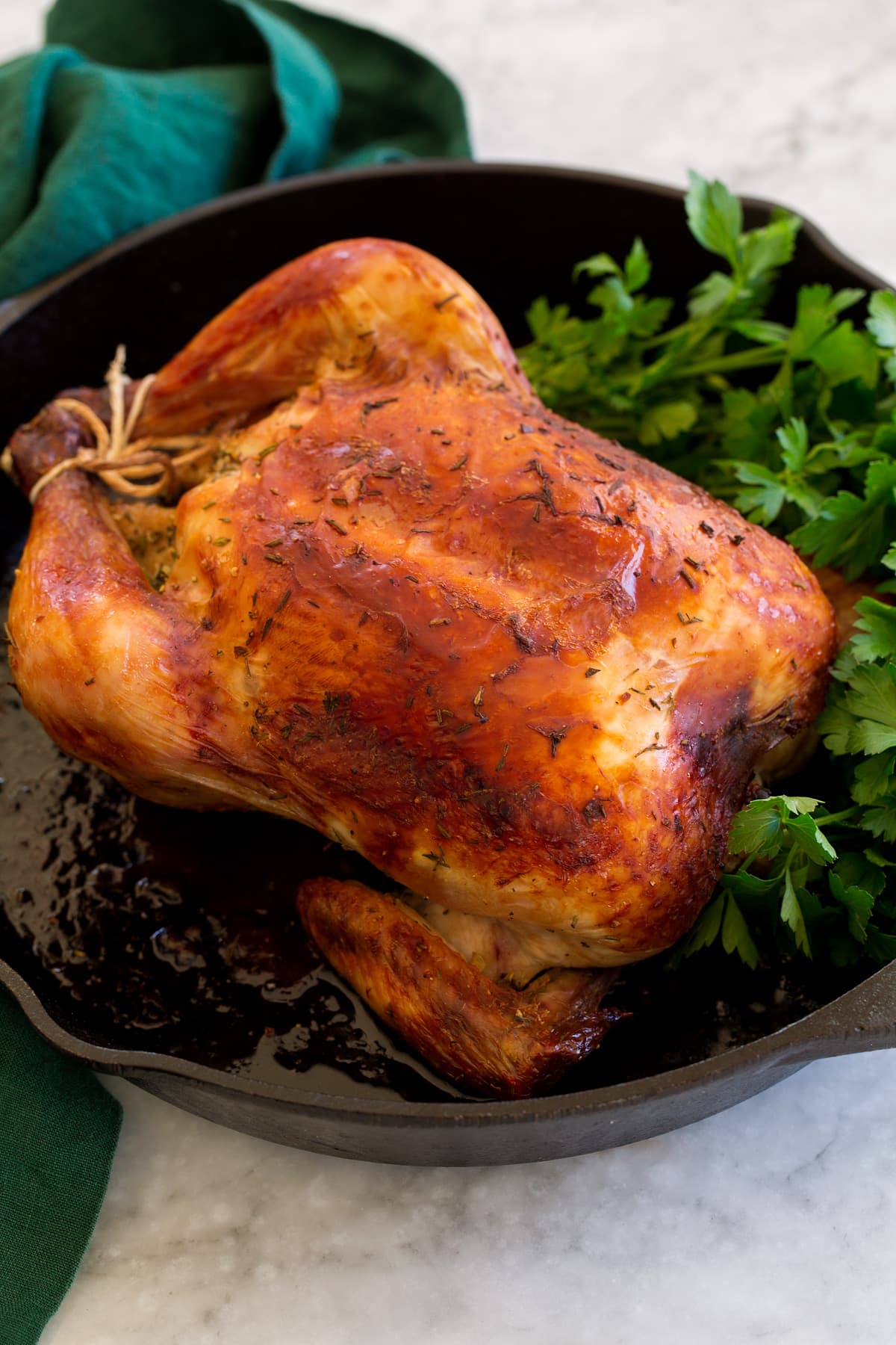 Whole roasted chicken shown in a cast iron skillet with fresh herbs.