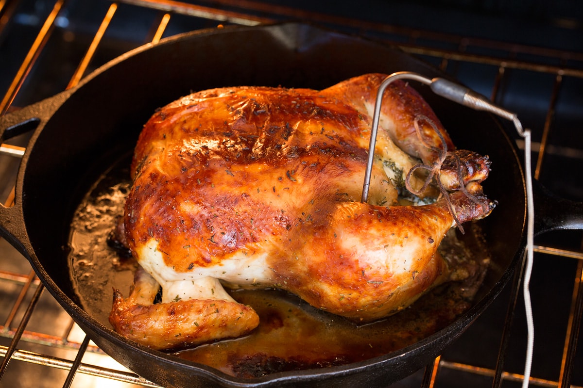 Photo of a browned whole chicken roasting in the oven with a food thermometer inserted into the thigh.