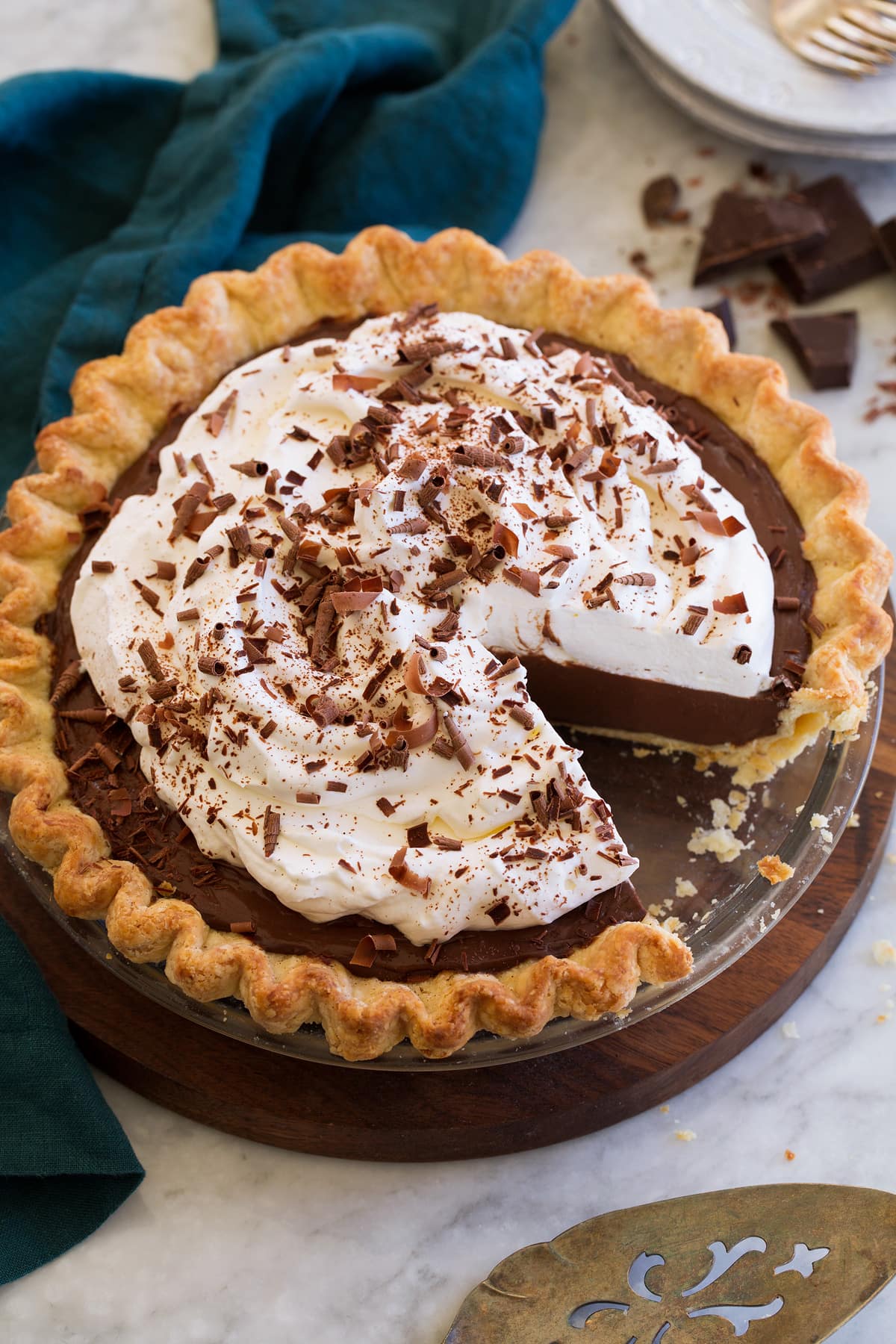Whole chocolate cream pie decorated with fluffy whipped cream and chocolate curls. One slice is cut from the pie to show the filling.