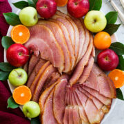 Sliced ham on a platter with fresh fruits and bay leaves.