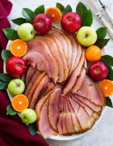Sliced ham on a platter with fresh fruits and bay leaves.