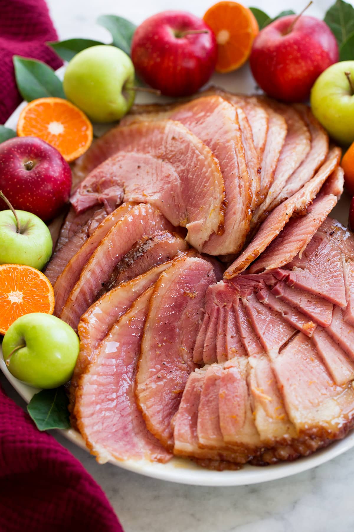 Spiral sliced ham that was cooked in a slow cooker shown on an oval white serving platter close up with decorative fruit and herbs to the sides.