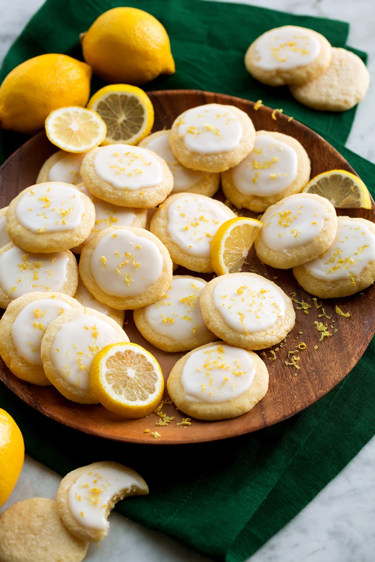 Lemon meltaway cookies shown on a wooden plate over a green cloth on a marble surface with lemons for decoration.
