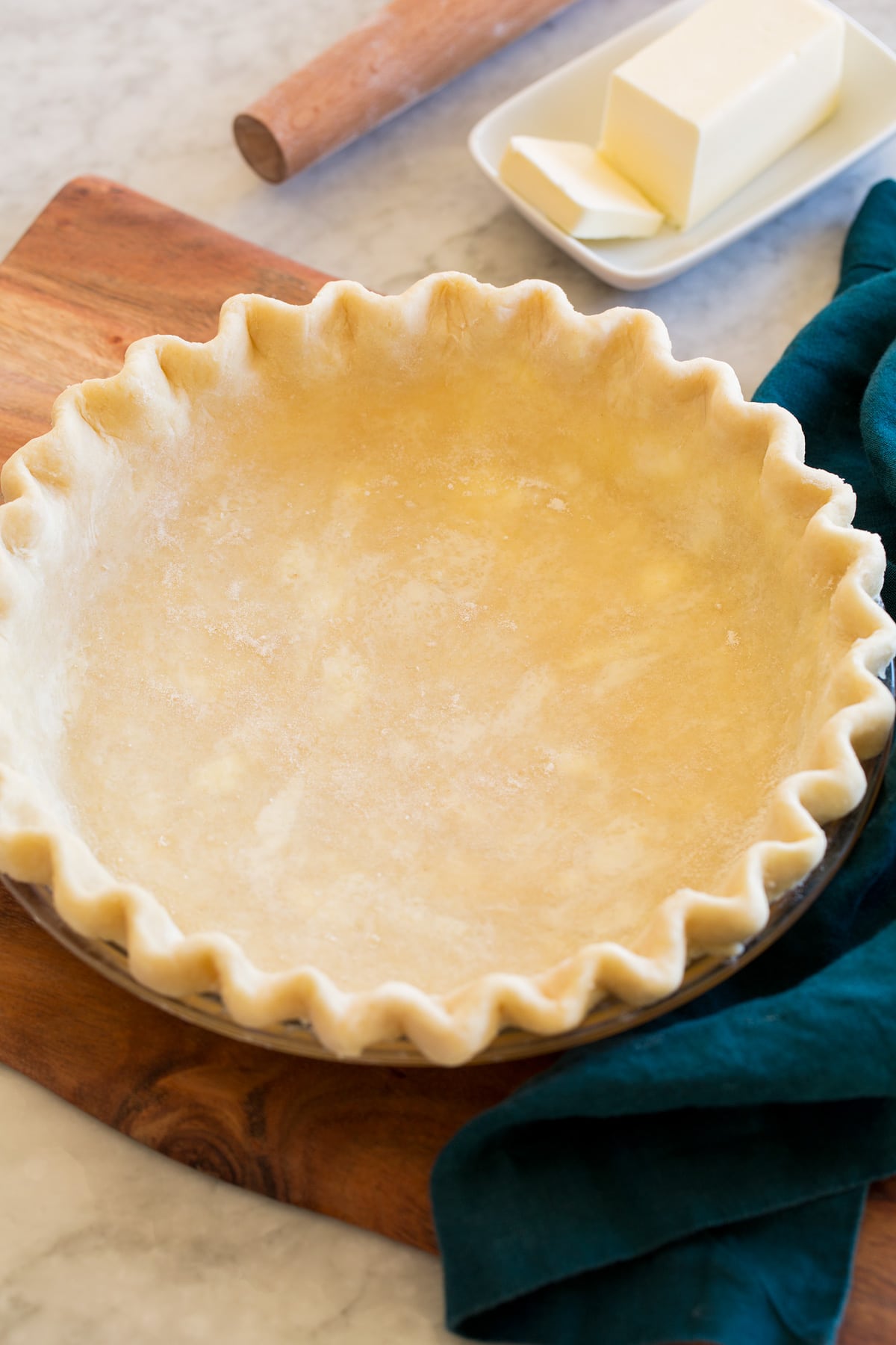 Pie Crust shown before baking in a glass pie pan set on a wooden platter.