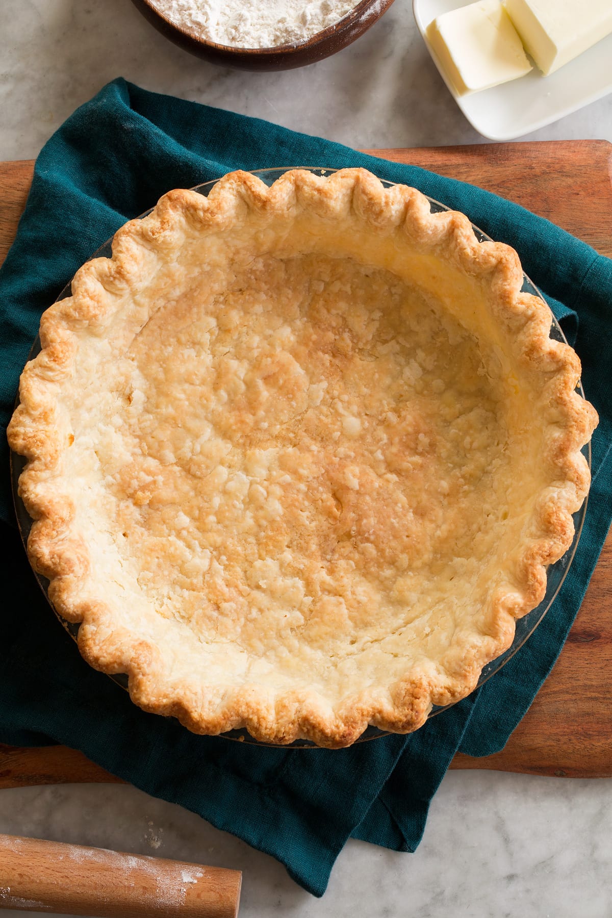 Blind Baked Pie Crust shown from above on a blue cloth and a wooden platter.