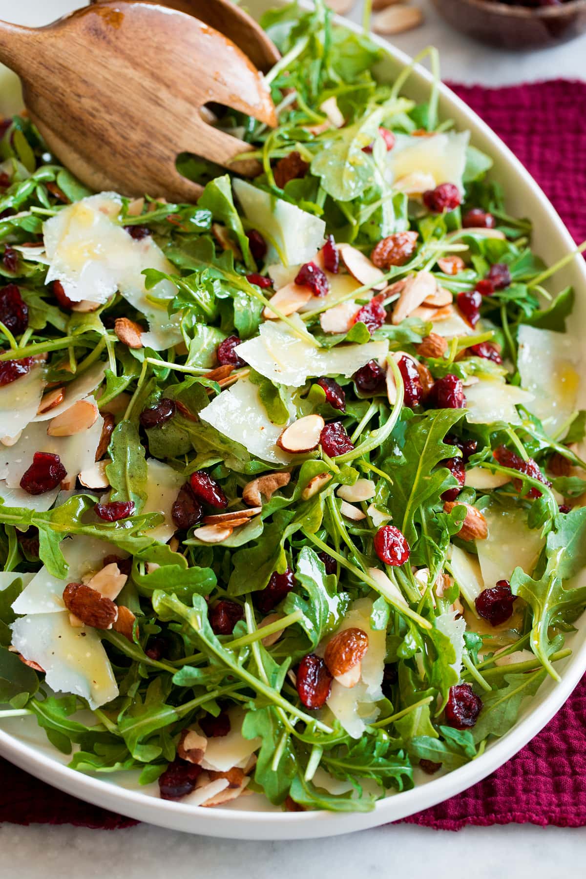 Arugula salad shown with salad serving spoons scooping salad.