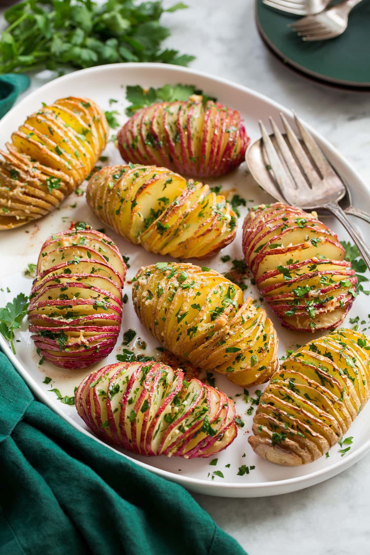 Hasselback potatoes on a serving platter on a marble surface with a green cloth.