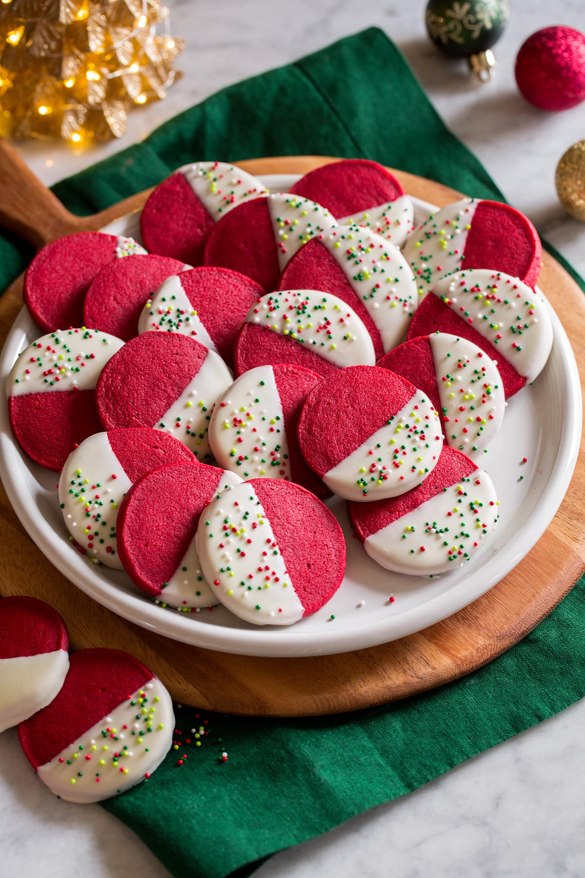 Red velvet shortbread Christmas cookies shown piled on a white serving plate over a wooden platter and a rich green cloth.